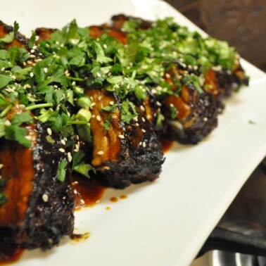 a white platter of Chinese short braised ribs topped with cilantro and sesame seeds