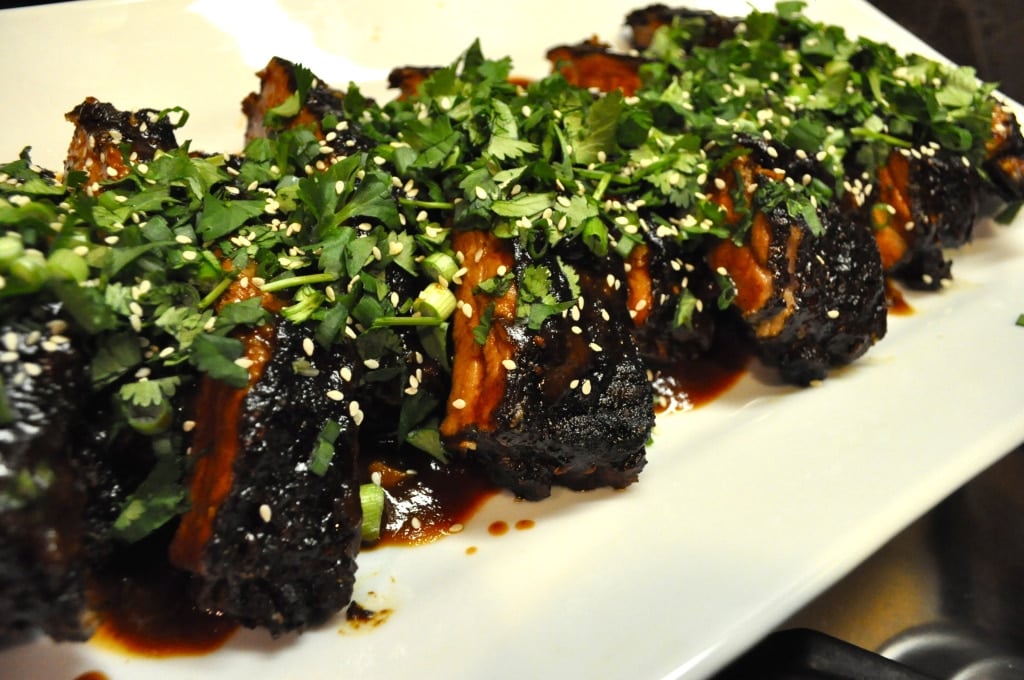  a white platter of Chinese short braised ribs topped with cilantro and sesame seeds
