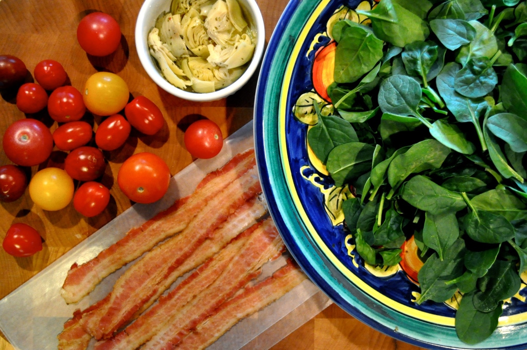 overhead view of a plate of spinach, bowl of artichokes, and cherry tomatoes