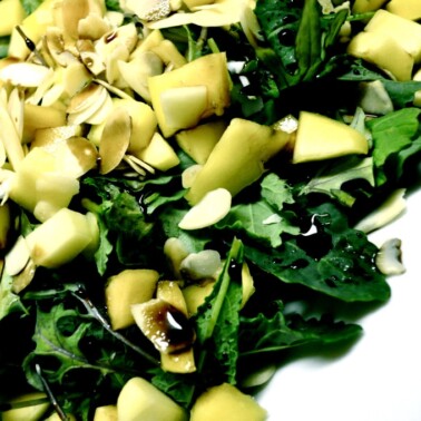 a pile of baby kale with diced mango, slivered almonds and dressing on top