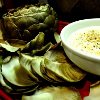 overhead view of cooked artichoke with a bowl of lemon artichoke dip