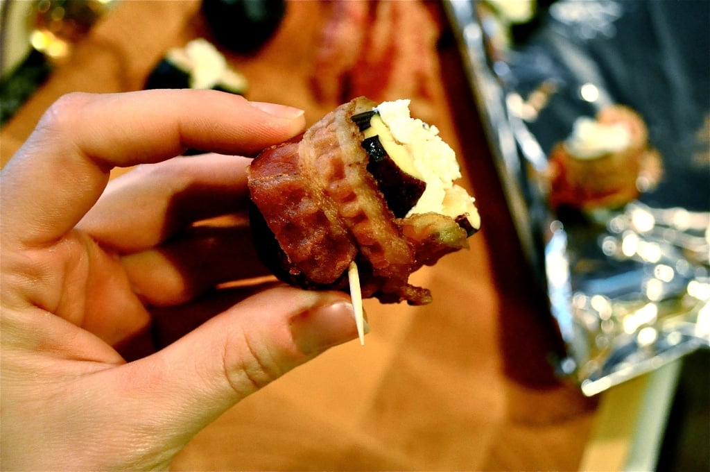 a hand holding a fig stuffed with goat cheese and wrapped in bacon