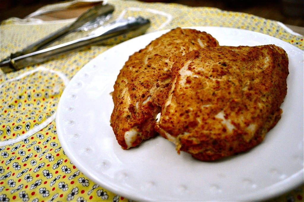 two baked mustard chicken breasts on a white plate on top of a yellow flower patterned napkin