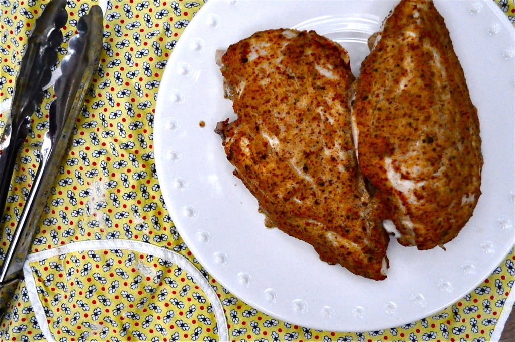 overhead view of two baked mustard chicken breasts on a white plate on top of a yellow flower patterned napkin