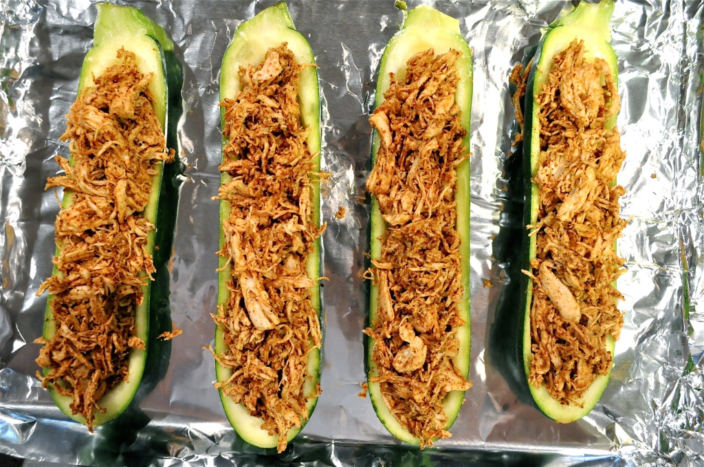 overhead view of hollowed out zucchini halves stuffed with shredded chicken and spices on a foil lined baking sheet