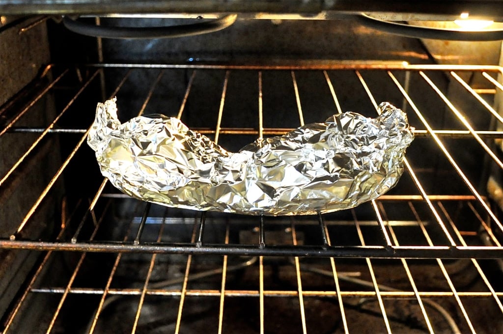 a peeled banana topped with almond butter wrapped in foil in the oven