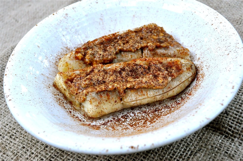 baked bananas in a white bowl topped with almond butter