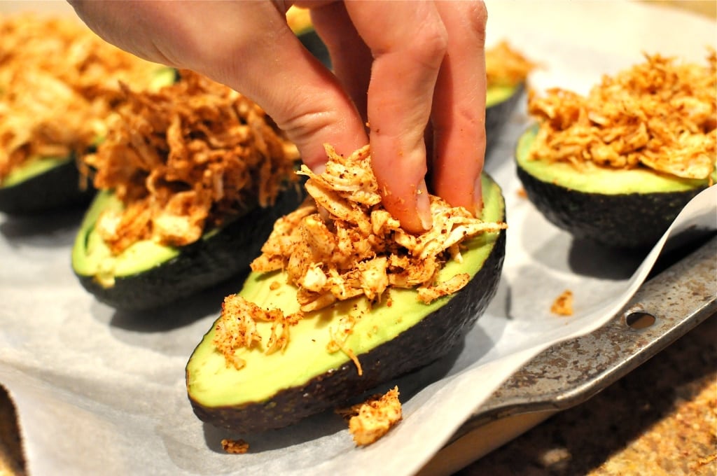 Shredded chicken being stuffed into avocados