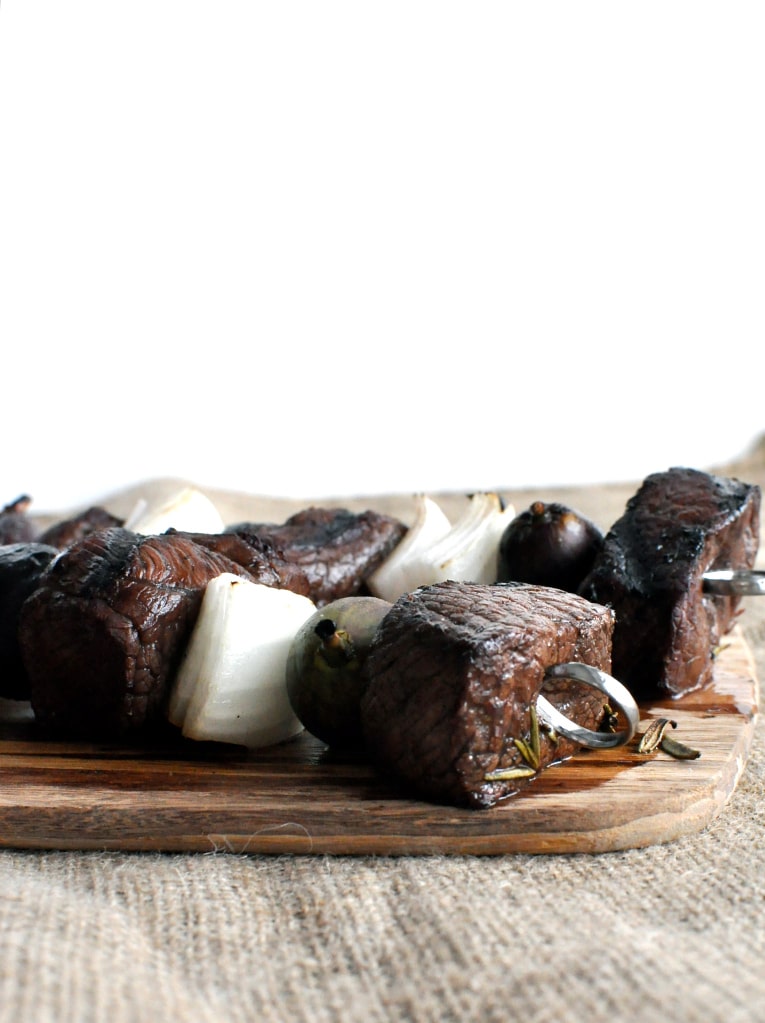 balsamic fig beef kabobs on a wooden cutting board on top of a burlap tablecloth