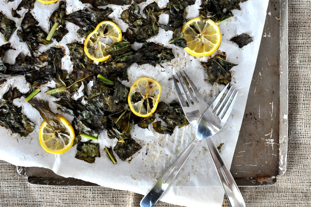 overhead view of charred turnip greens and lemon slices on parchment paper and a sheet pan