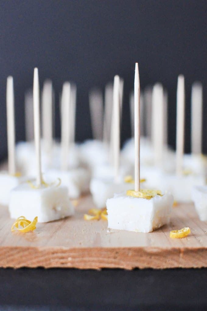 multiple squared white lemon vanilla meltaways garnished with lemon zest and stuck with toothpicks on top of a wooden board
