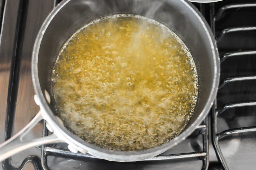 orange juice and honey bubbling in a black saucepan on a gas stovetop