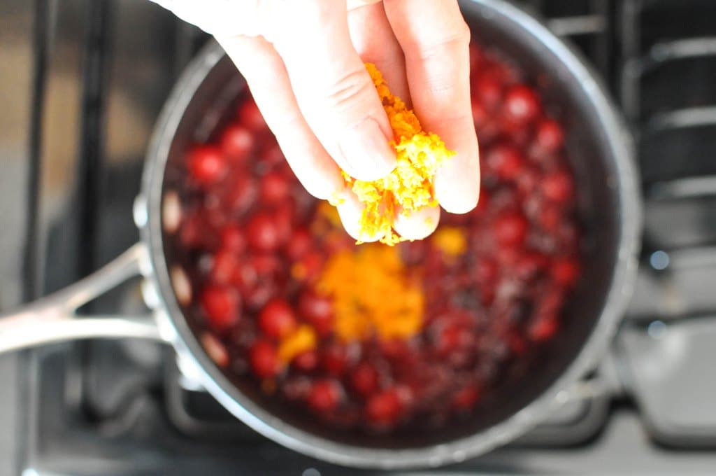 woman's hand sprinkling orange zest into a pot full of cranberry sauce