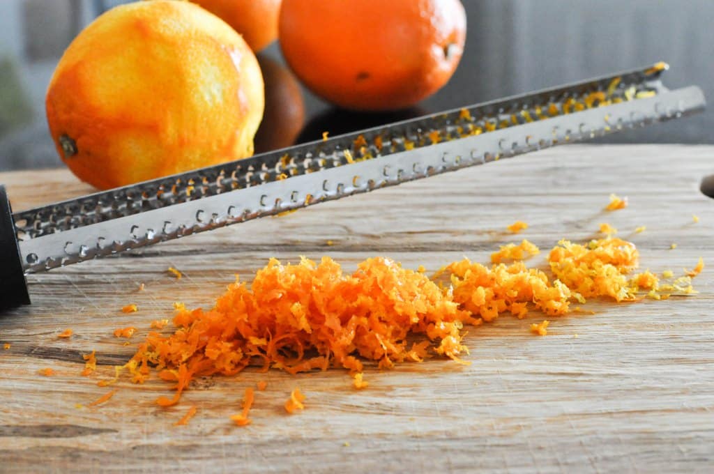 orange zest on a wooden cutting board with a microplane hovering over it