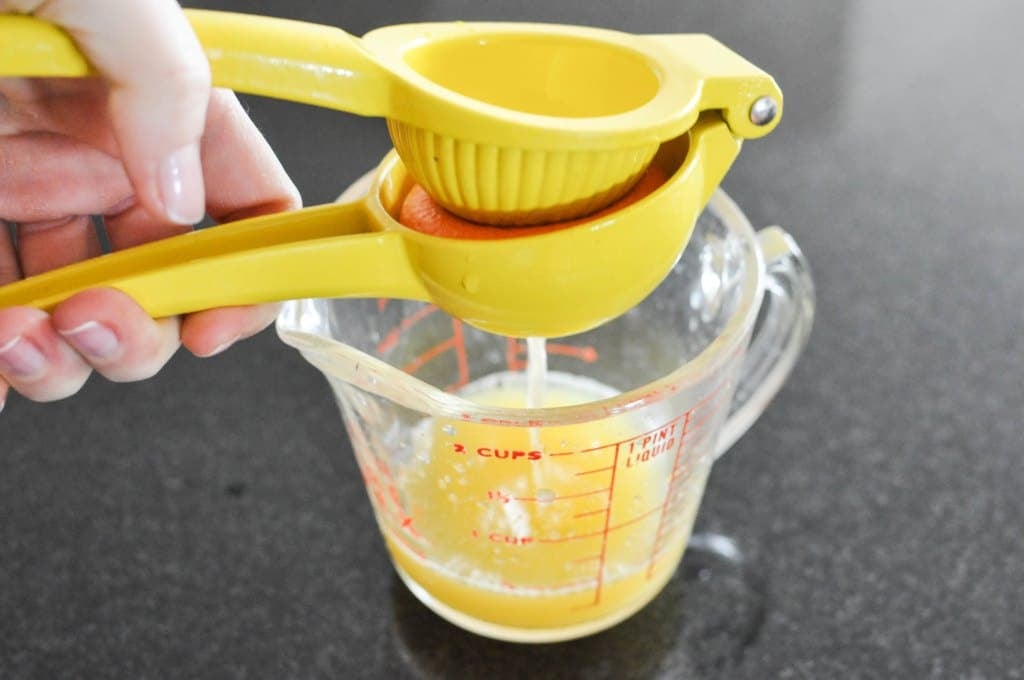 an orange half in a lemon squeezer being juiced into a glass measuring cup