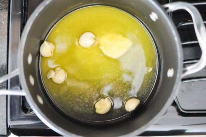 six cloves of garlic being cooked in melted butter in a grey pot on the stovetop