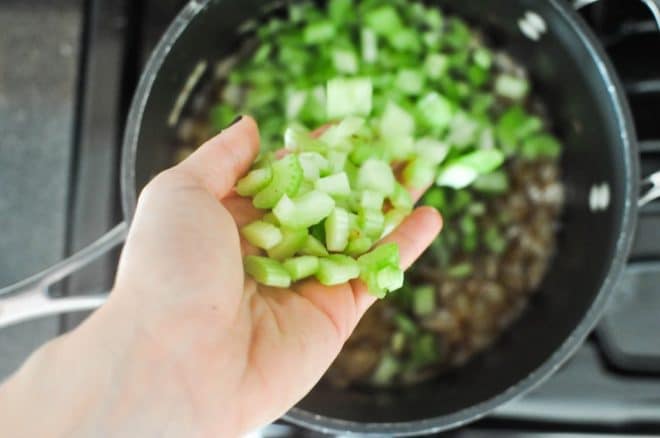 chopped celery being added to a grey pot with diced onions