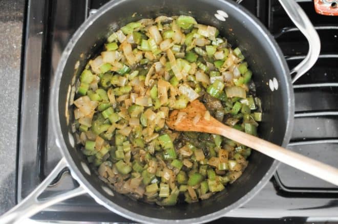 diced onions and celery in a grey pot with seasonings and a wooden spoon