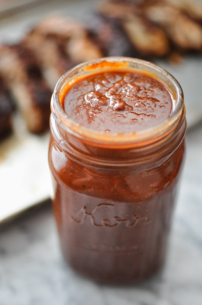 mason jar full of paleo barbecue sauce on a marble table with ribs blurred in the background