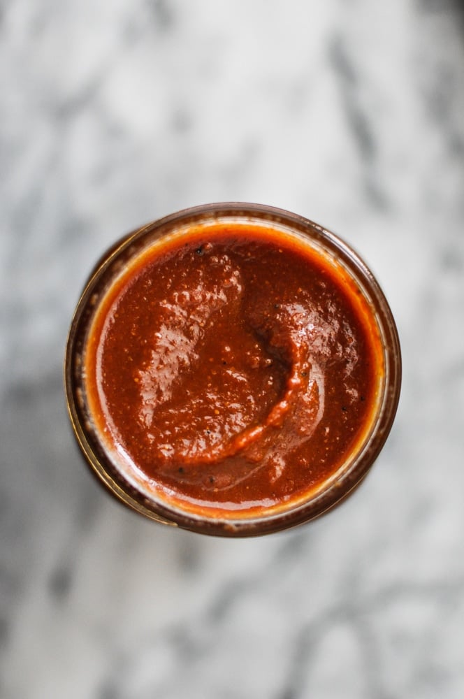 overhead view of glass mason jar filled with red paleo barbecue sauce on a marble tabletop