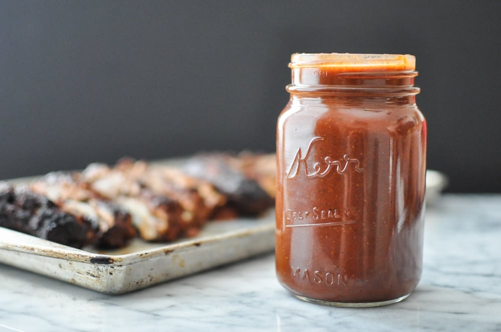 mason jar full of paleo barbecue sauce on a marble table with ribs blurred in the background