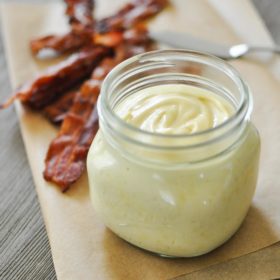 a glass jar of baconnaise on top of parchment paper with cooked bacon in the background