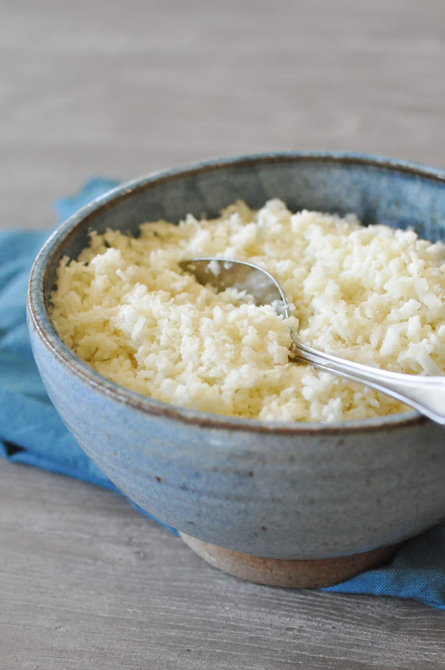 basic cauliflower rice in a blue bowl with a blue napkin on top of a grey wooden table