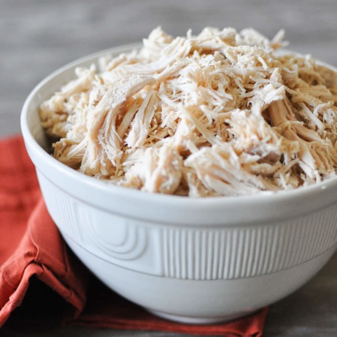 a white bowl on top of a red napkin sitting on a grey wooden table filled with cooked shredded chicken