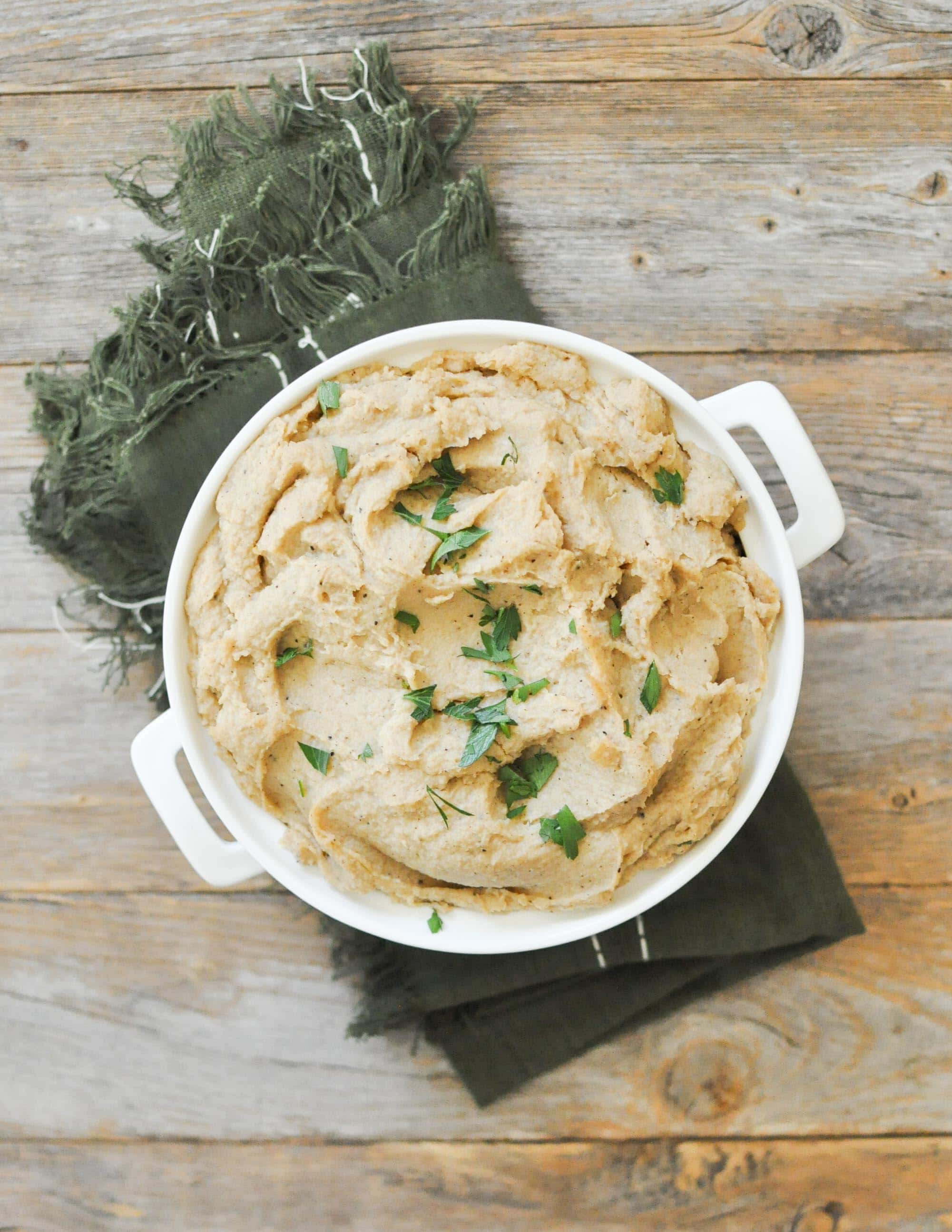 overhead view of a white casserole dish filled with browned butter parsnip mash on top of a green napkin on a wooden table