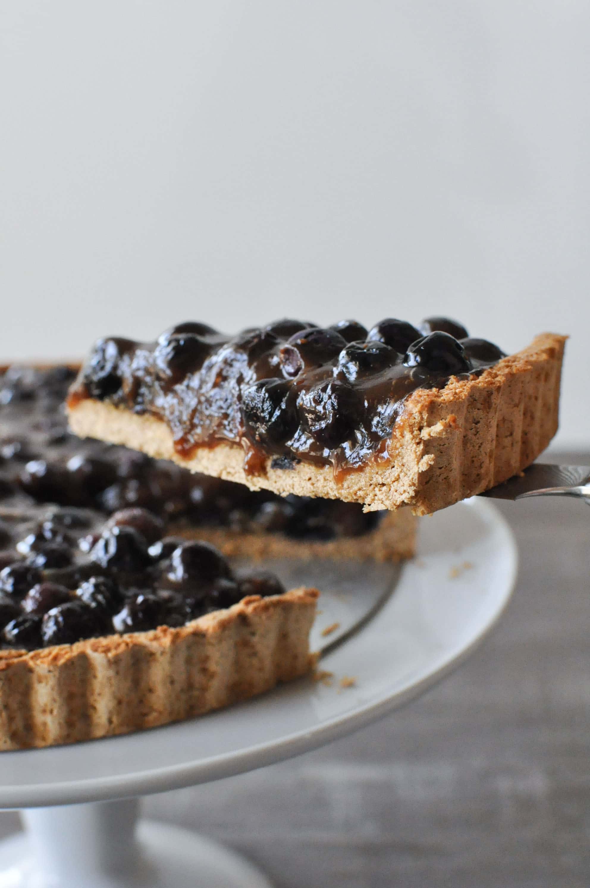 a slice of blueberry tart being lifted from a plate of blueberry tart with a pie cutter