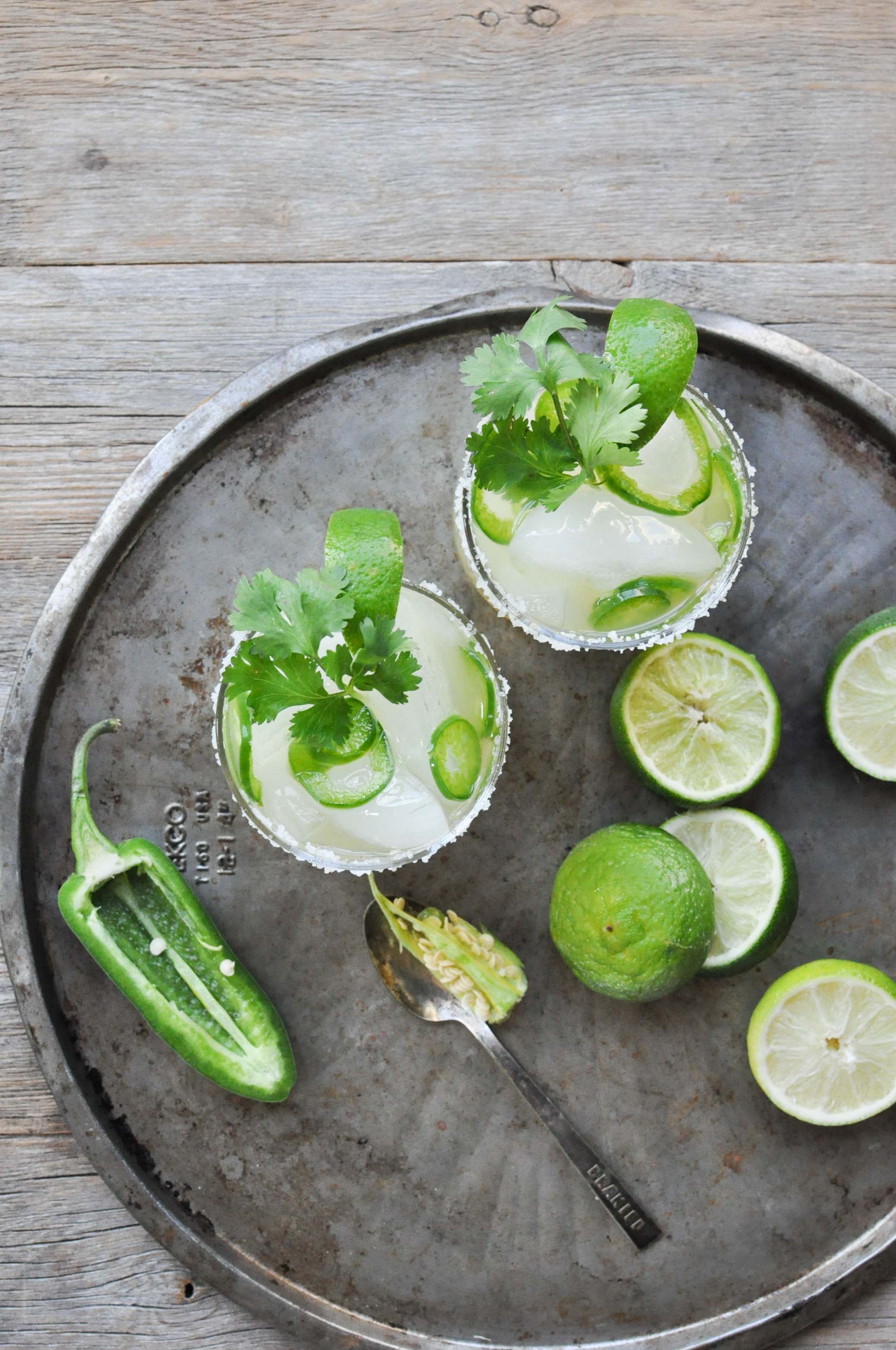 two margarita glasses filled with a fresh jalapeno and lime margaritas and garnished with a salt rim, limes, and cilantro