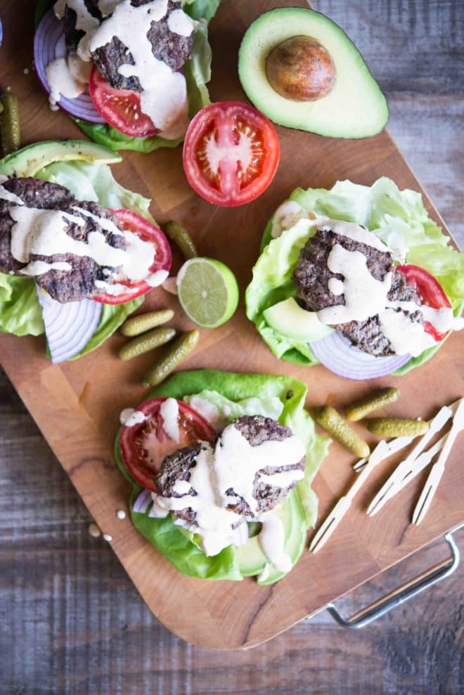 overhead view of beef sliders on top of lettuce, red onion, and tomato slices with chipotle lime mayo drizzled on top