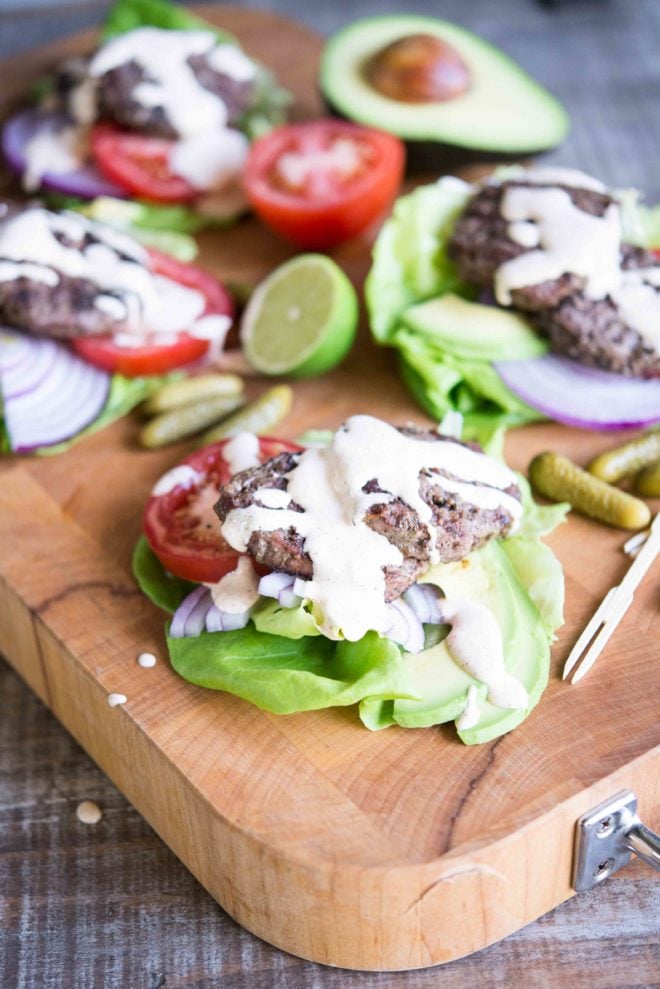 beef sliders on top of lettuce, red onion, and tomato slices with chipotle lime mayo drizzled on top