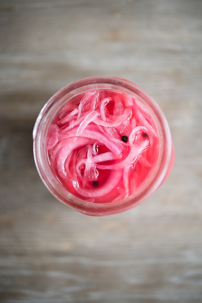 overhead view of a mason jar full of pink pickled red onions on a wooden table