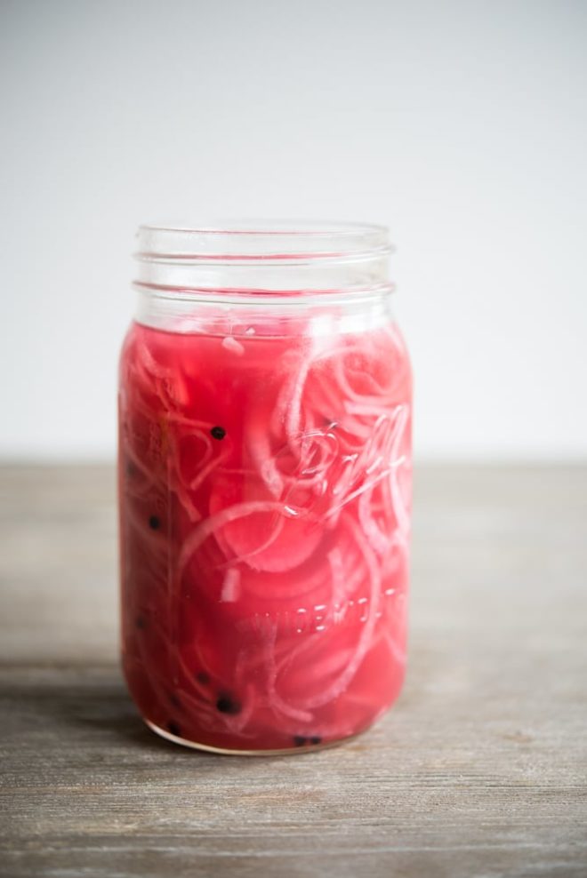 a mason jar full of pink pickled red onions on a wooden table