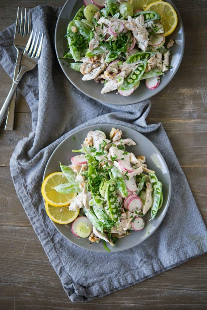 overhead view of two gray bowls full of chicken salad with snap pea radish slaw on top of a gray napkin