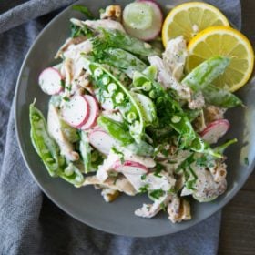 overhead view of a gray bowl full of chicken salad with snap pea radish slaw on top of a gray napkin