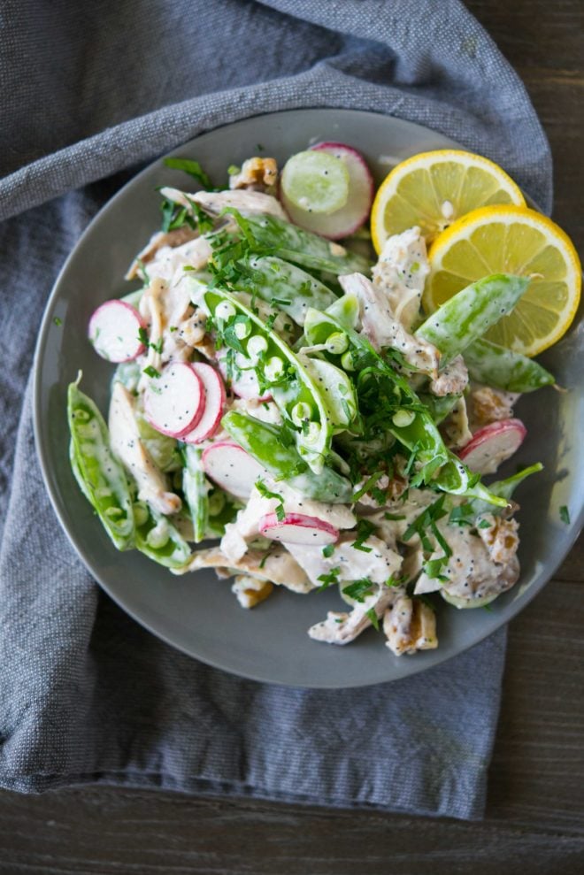a gray overhead view of a bowl full of chicken salad with snap pea radish slaw on top of a gray napkin