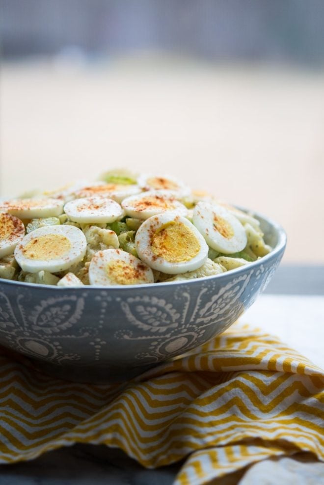 bowl of Cauliflower "Potato" Salad with zig zag yellow napkin on a marble tabletop