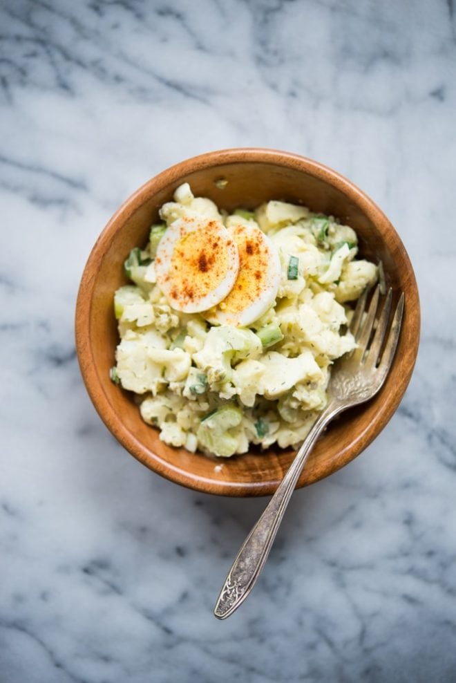 overhead shot of bowl of Cauliflower "Potato" Salad on a marble tabletop