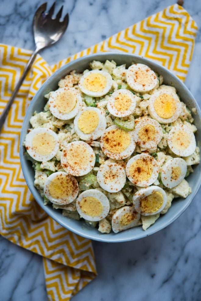 overhead shot of bowl of Cauliflower "Potato" Salad with zig zag yellow napkin on a marble tabletop