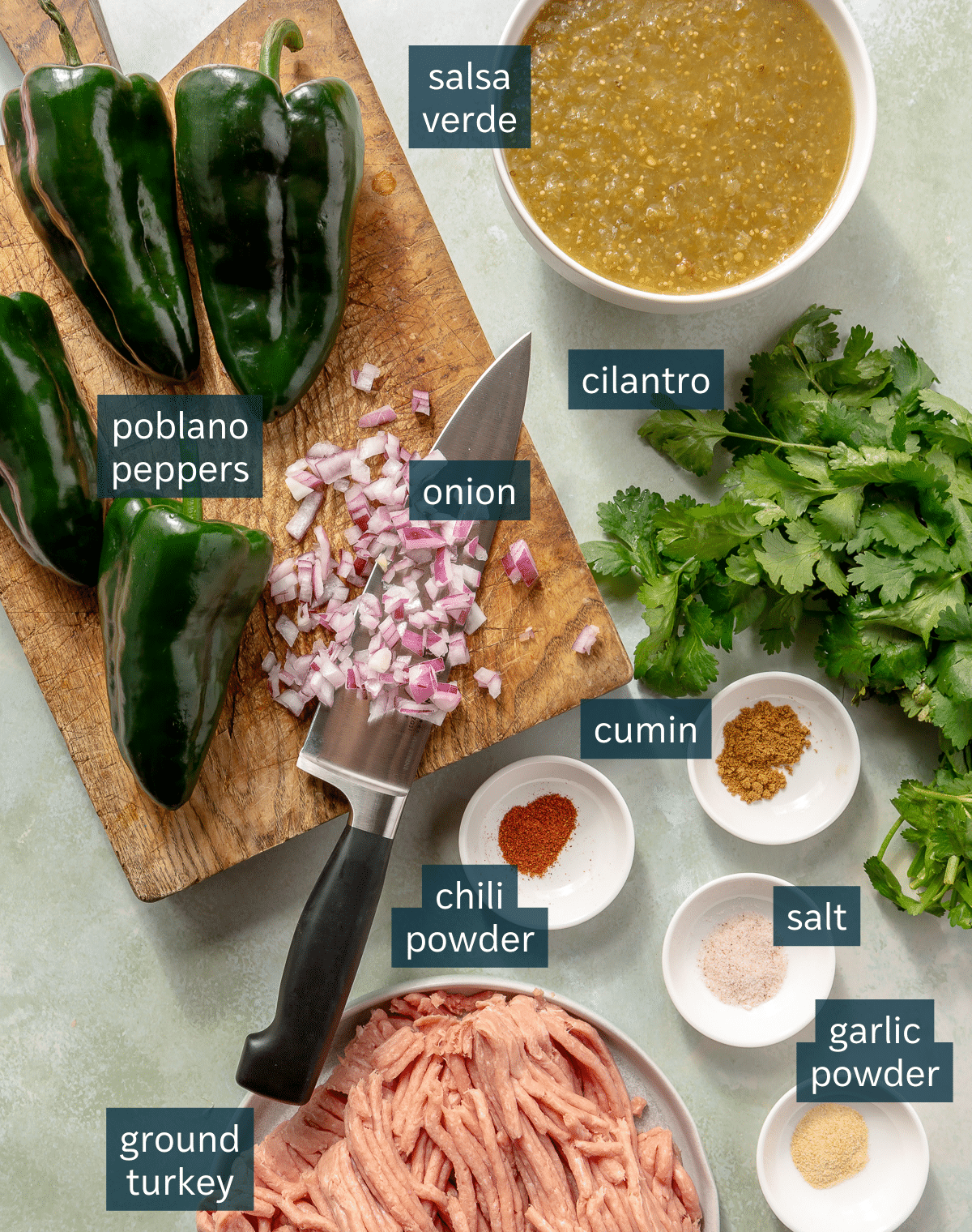 Ingredients for enchilada verde turkey meatballs sit in a variety of bowls and on a wooden chopping block.