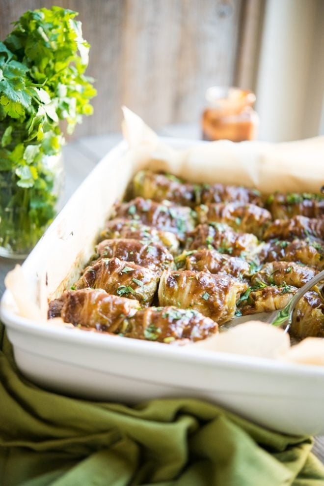 a white casserole dish filled with asian cabbage rolls and garnished with chopped cilantro