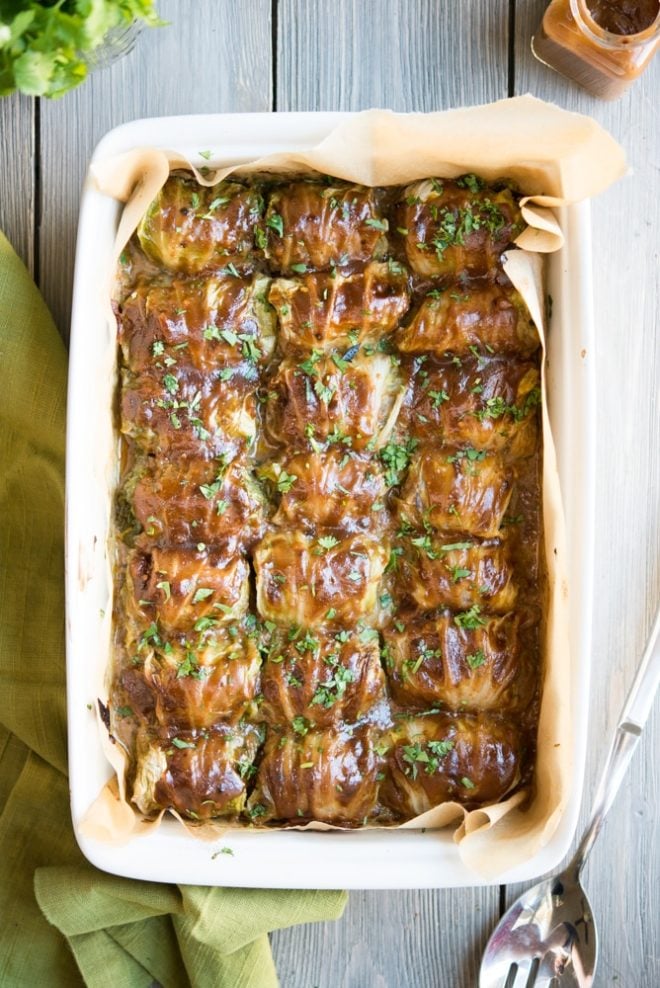 a white casserole dish filled with asian cabbage rolls and garnished with chopped cilantro