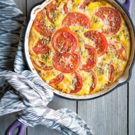 Enameled skillet with tomato frittata on a wooden surface.