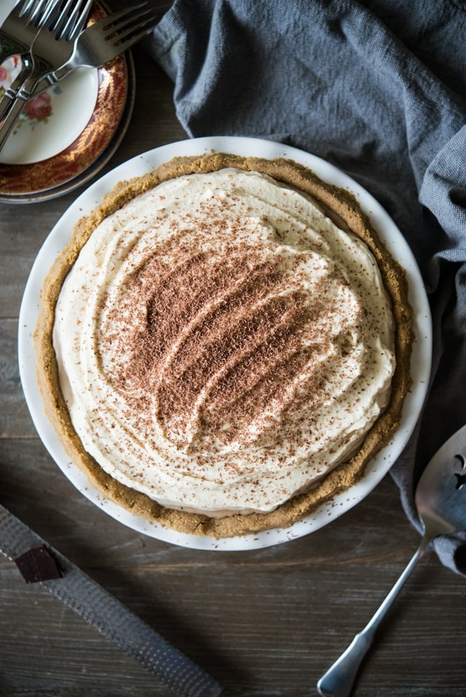 overhead view of chocolate mousse pie topped with whipped cream and chocolate shavings in a graham cracker crust in a white ceramic pie tin on a wooden surface