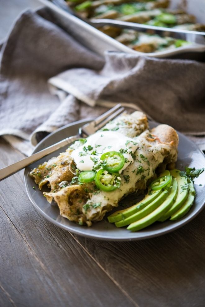 a plate of chicken enchiladas verde with slices of avocado