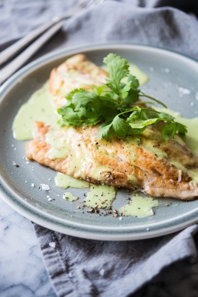 Pan Fried Butter Snapper topped with cilantro cream sauce and fresh cilantro leaves on a gray plate