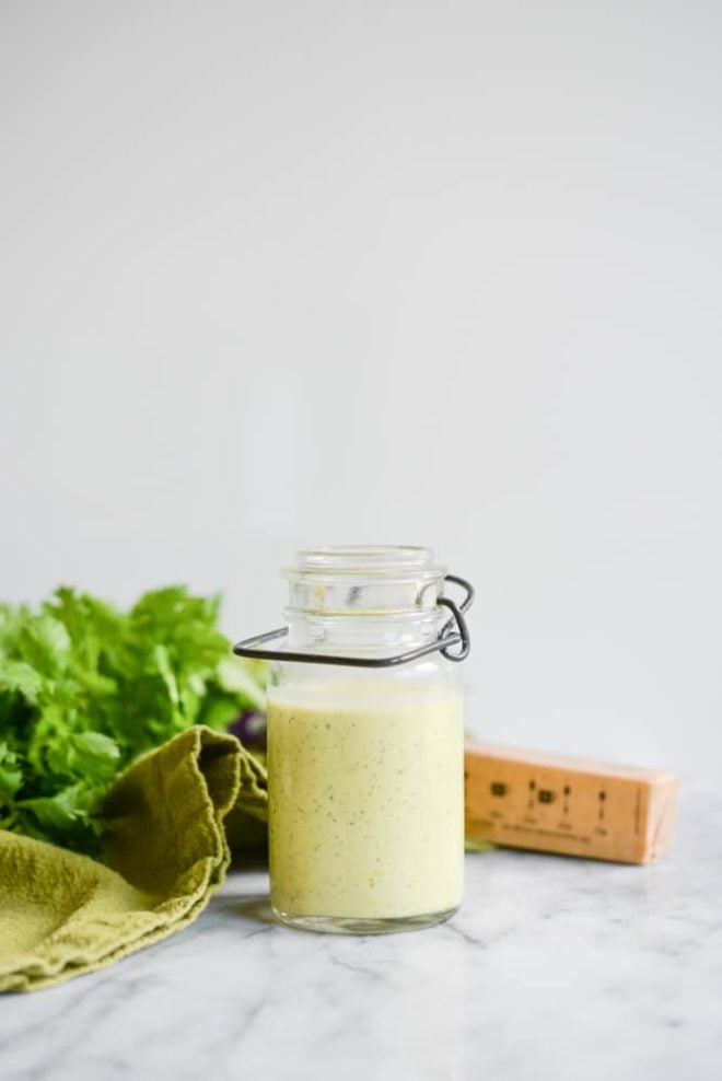 glass jar of cilantro hollandaise sauce on a white marble table with cilantro in the background