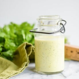 glass jar of cilantro hollandaise sauce on a white marble table with cilantro in the background